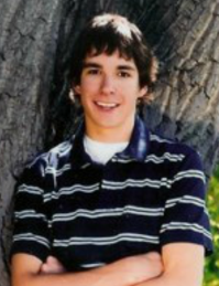 Senior picture of Michael, wearing golf shirt, with back on tree, smiling at camera.