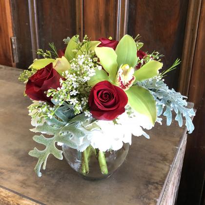 Bubble bowl with white hydrangea, three red roses, three green orchids, dusty miller, and filler.