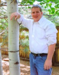 Matthew's senior picture, with arm on aspen tree to his right, smiling, looking back at camera