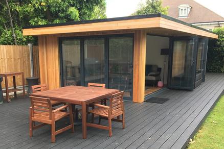 Modern cedar clad garden room with 2 sets of bifold doors and a table and chairs in front on a large decking area