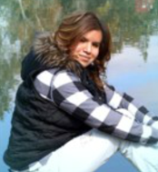 Outdoor picture of Karina, sitting, turning her head to her right, looking at camera.