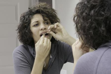 Model demonstrates the difficulties of flossing your teeth using traditional methods: messy, difficult to grip of hold the floss.
