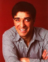 Nijat's senior picture, arms crossed on table, smiling, looking at camera