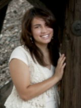 Outdoor picture of Carissa, leaning on tree, smiling at camera.