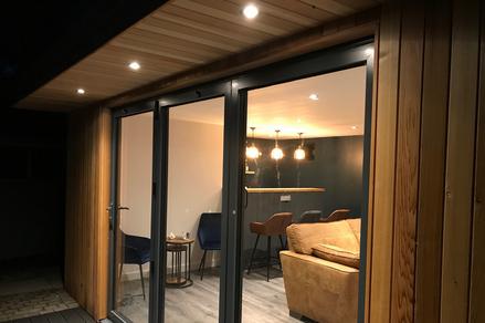 Modern cedar clad garden room at night showing a lit bar area