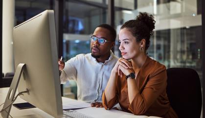 Two professionals seating at a desk looking at a computer.
