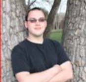 Outdoor picture of Zach, standing against a tree, wearing sunglasses.