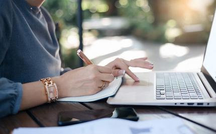 woman typing on a laptop and taking notes