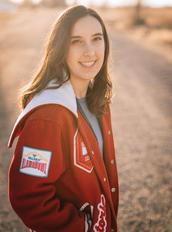 Victoria, outdoors wearing letter jacket, smiling, looking at camera.