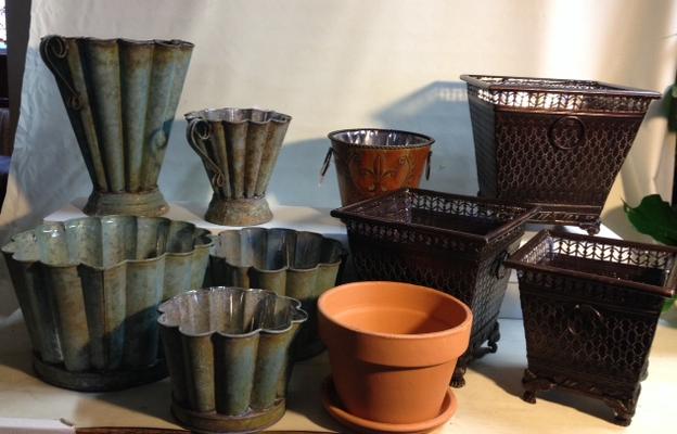 Gray hammered tin, mahogany checked metal, and brown fleur de lis containers next to a terra cotta pot