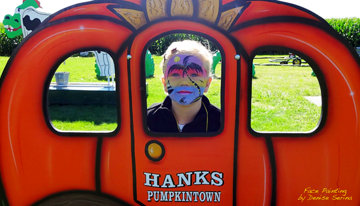 Child with an Island Scene painted on his face standing behind a Pumpkin Carriage Photo Op at Hank's PumpkinTown