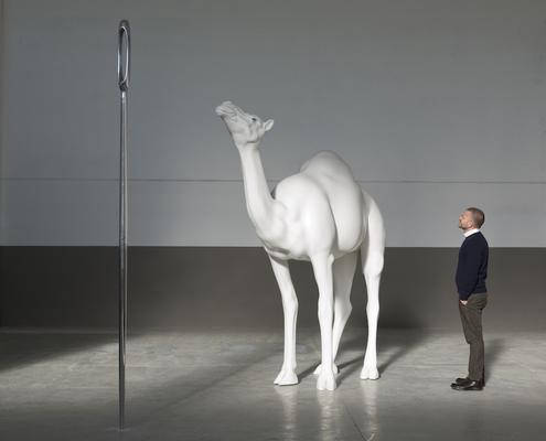 Man staring at sculpture of tall needle, large camel