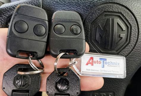 2 Lucas remote fobs above 2 MG keys in front of an MG steering wheel.