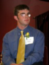 Joshua, sitting in chair at 2004 STF reception, wearing shirt and tie, looking to his left.