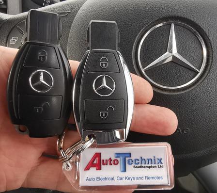 Picture of a Mercedes key and a Replacement Mercedes key both Chrome style 2 button remote key in front of a Mercedes steering wheel with the Mercedes emblem to the right of the picture
