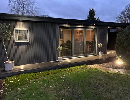 Garden room with black cladding 3 panel bifold doors and a small square window