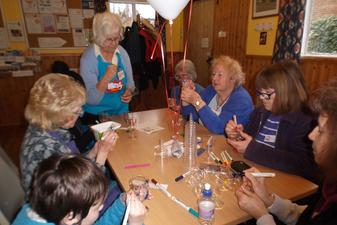 Seven people around a table decorating candle holders, with a balloon in the centre of the table.
