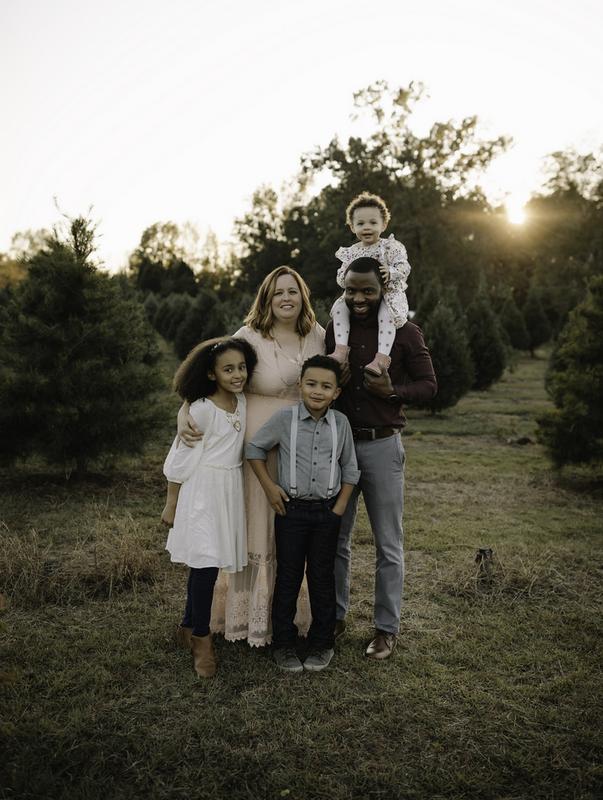 Adorable family at a Christmas tree farm with sun setting in the background.