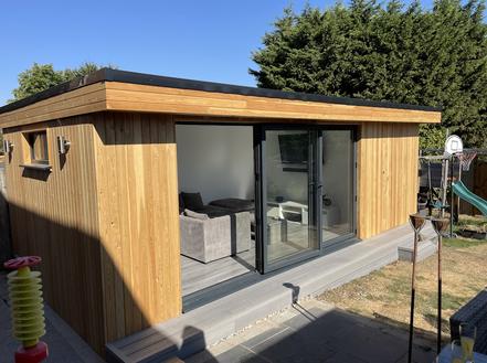 Modern cedar clad garden office with open 3 panel bifold doors and integral shed
