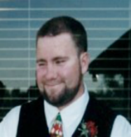 Head-shot of Derek, wearing tie & vest, looking down.