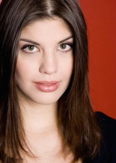 Color photo of spinto soprano Megan Marie Hart with straight, shoulder-length hair against a dark red background. She is looking into the camera, her lips slightly parted.