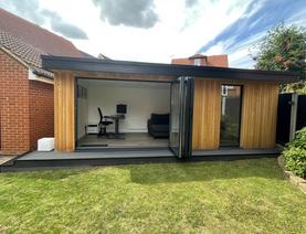 Cedar clad garden room with a full length window and open bifold doors showing an office desk and chair