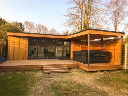 Modern cedar clad garden room with 5 panel bifold doors and a hot tub under a canopy