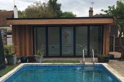 Modern cedar clad pool house garden room with 5 panel bifold doors behind an outdoor swimming pool