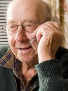 Image of older male adult wearing green sweater and glasses making a telephone call on his mobile device.