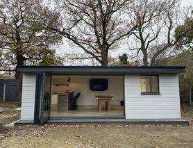 Grey composite clad garden room with small window and open bifold doors showing a bar, TV and pool table