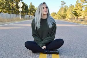 Aliah sitting in the middle of a quiet, tree lined road, looking up and to her left.