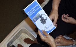 An "Ioncleanse Detox" brochure being passed from one hand to the other as feet are in the small tub of water