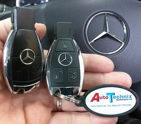 Picture of a Mercedes key and a Replacement Mercedes key both Chrome style 3 button remote key in front of a Mercedes steering wheel with the Mercedes emblem to the right of the picture
