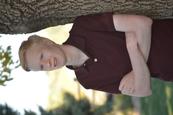 Ryan Long, standing with arms crossed, looking slightly to his right, smiling outdoors next to a large tree