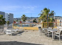 View of Sutro Tower in the distance, palm tree close to building, chairs and table.