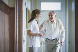 Nurse speaking with resident as he walks down a hallway with his walker