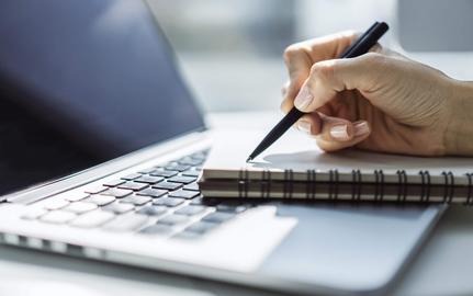 Image of a hand with notebook, pencil, and laptop