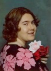 Amy holding flower on chest, facing let, looking right.