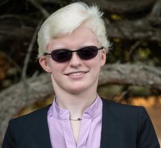 Pamela smiling at the camera wearing sunglasses with natural, outdoor backgorund.
