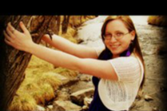 Outdoor picture of Kayla hugging a tree and smiling at camera