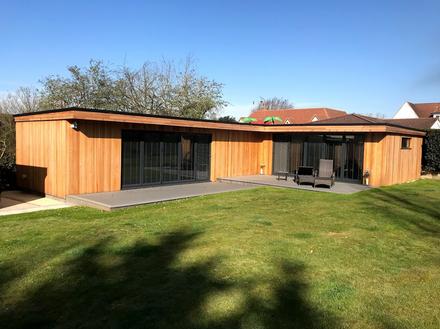 Large dual aspect cedar clad garden room with bifold doors and decking area with lounge chairs