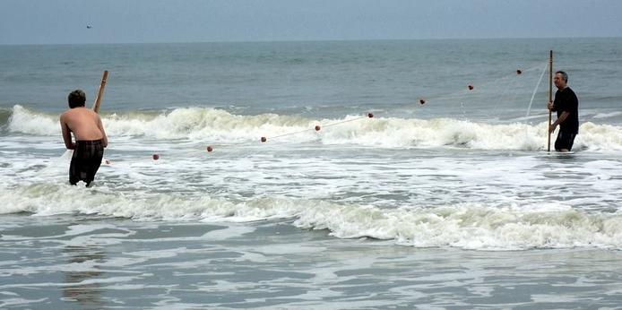 Two men holding a seine net in the surf