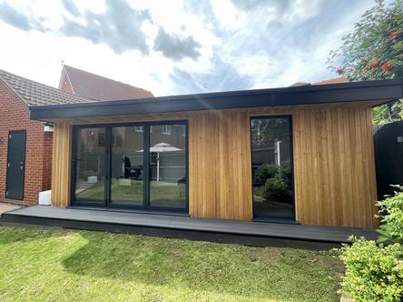Modern larch clad garden office with 3 panel bifold doors and full length window