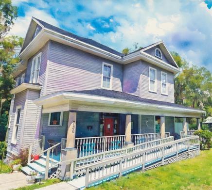 Soft watercolor painting of the CATS (Comprehensive Addiction Treatment Services) office building in Ocala, a welcoming two-story gray house with white trim, a spacious wraparound porch featuring blue chairs, and a bright red front door. The house number 730 is displayed on a porch pillar. The scene includes a vibrant green lawn, surrounding trees, and a bright blue sky with soft clouds, rendered in a gentle, artistic watercolor style with blended colors and delicate brushstrokes.