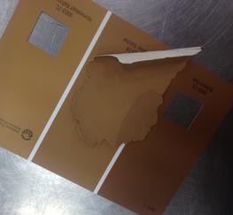 A large chip of paint sits on top of a color card featuring three different browns from the paint store. The paint chip has a brown splotch on one side which was an attempted color match, but its medium brown color is quite far off from the original light brown paint sample. The sample sits on top of the middle brown on the paint color card, which appears to be a near perfect match, found with the painter's naked eye.