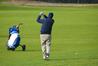 Golfer swinging club on fairway with a pull cart.