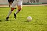 male soccer players legs on green field kicking soccer ball