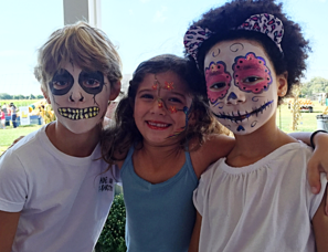 Three children with they're faces painted. The Boy on the left has a full face of skeleton facepaint. The girl in the middle has a stem with little flowers coming down her forehead and nose and across her right cheek. And the girl on the right has a full face of female skeleton facepaint with pink flowers around her eyes.