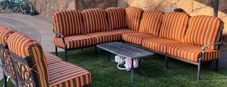 red, brown and orange striped wrought iron sectional and chairs with center table on green grass 