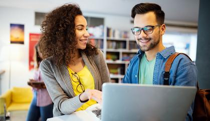 Two college students standing holding a laptop and talking